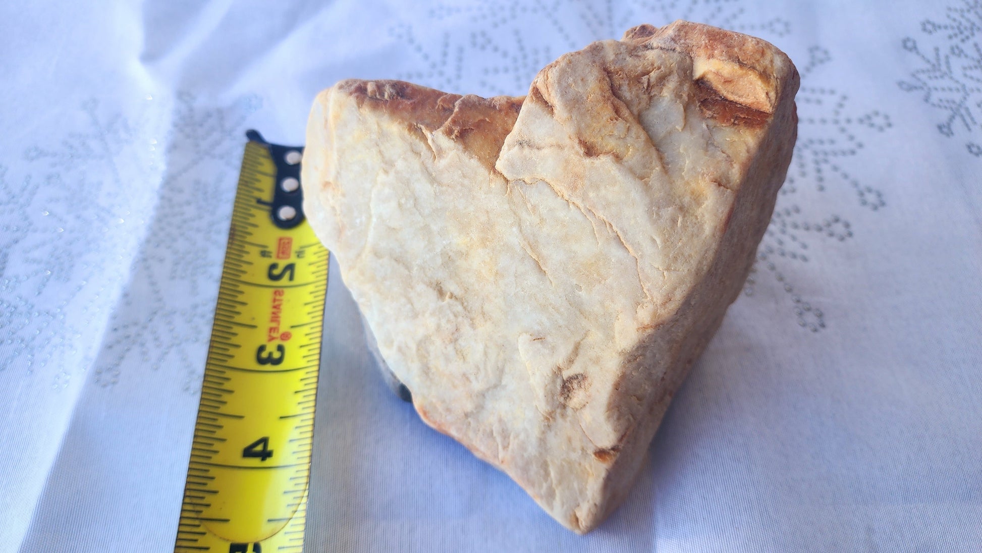 Natural heart-shaped rock with creamy white and golden tones, unpolished, resting on white fabric