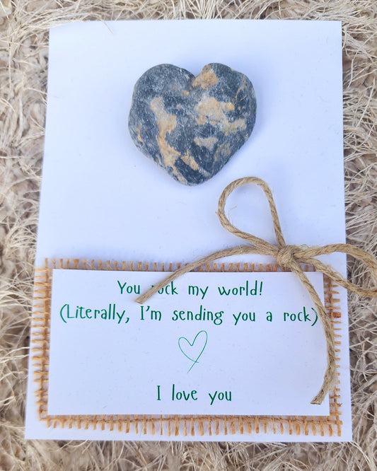 Heart-shaped stone on a card with text, tied with twine, on a textured surface