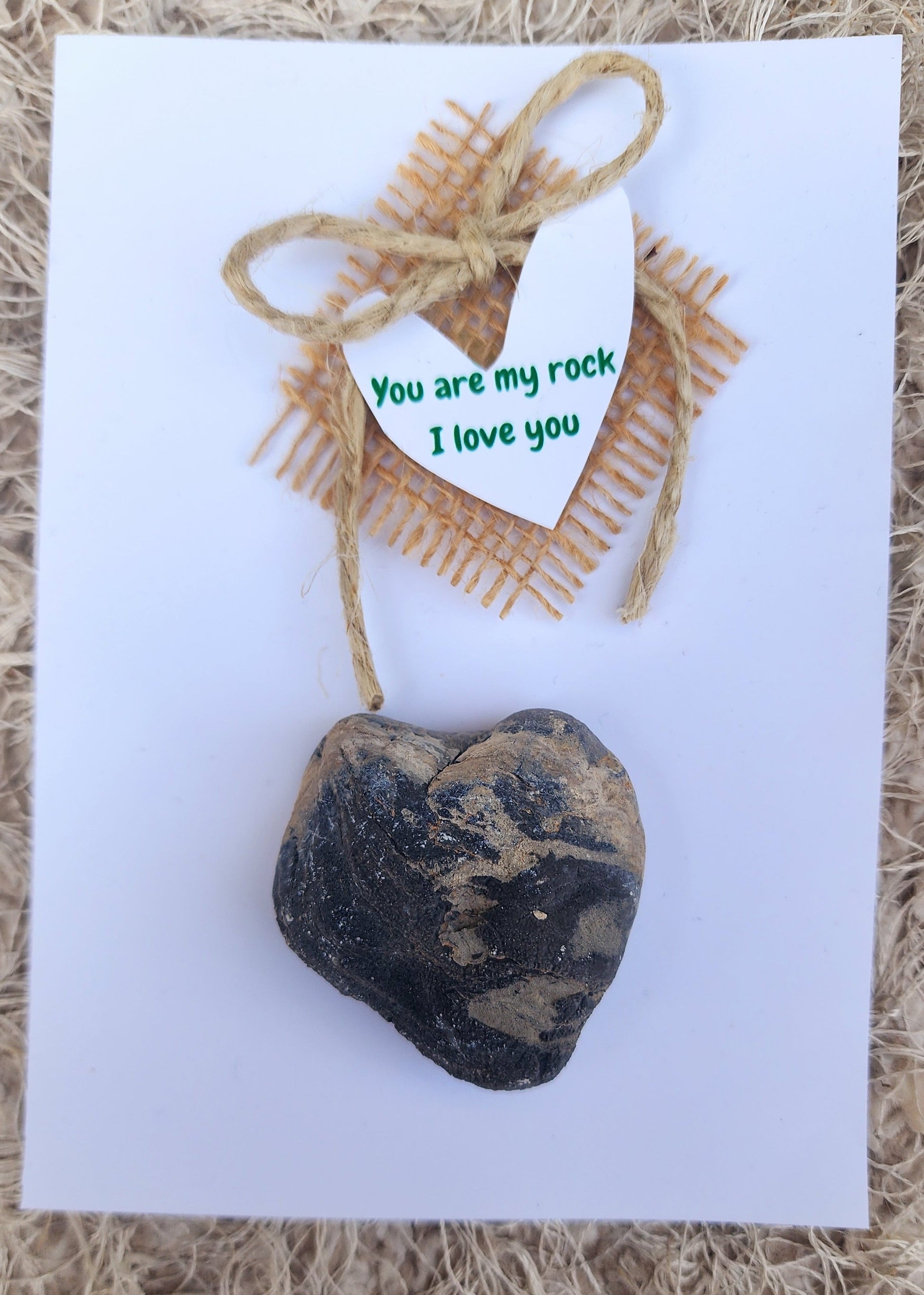 Heart-shaped stone on a white card with a small gift tag, all on a textured brown surface.