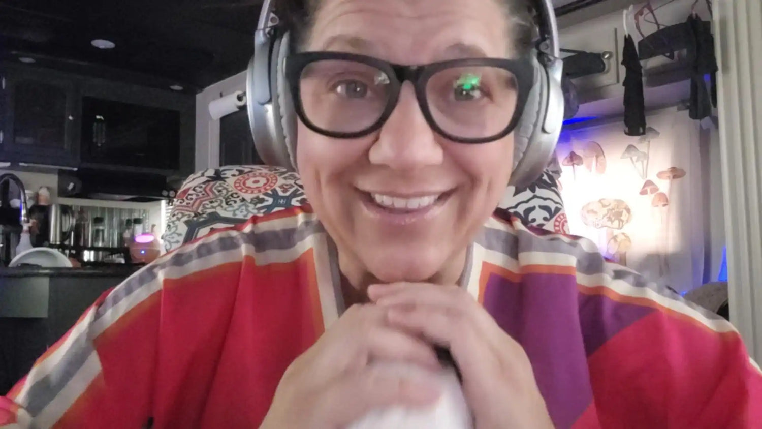 A smiling woman wearing headphones and glasses, with a colorful patterned top.